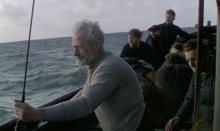 A still of a group of men on a boat, the ocean behind them